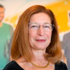 Leslie Hyman standing in front of a mural showing three people.