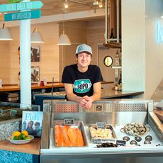 Lucas Myers behind the fish counter at SoPo Seafood. Display shows different kinds of fish and shellfish.