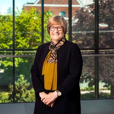 woman with short blonde hair and glasses standing in front of window