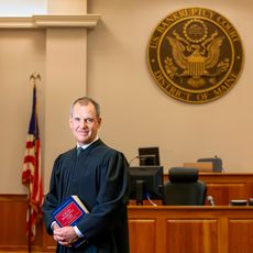Judge Peter Cary in his courtroom, holding a thick book of the Bankruptcy Code