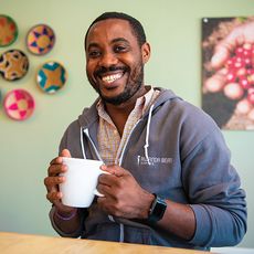 A man, black, holding a large coffee cup and smiling