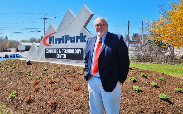  A man, smiling, stands outdoors in front of a sign that says FirstPark Commerce and Technology Center.