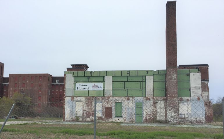 A delapidated brick industrial building with a smokestack and a sign that says future home of museum L-A