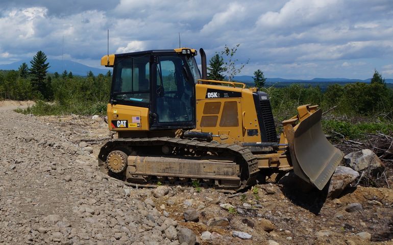 A bulldozer sits atop a hill, with mountains in the background