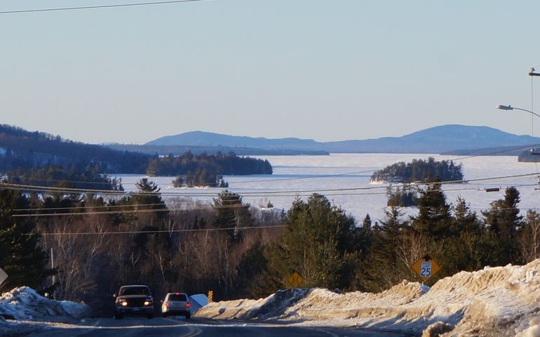 Trucks on a snowy road with a lake and mountains in the backround