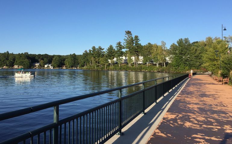 A boat on a lake with a man fishing off a boardwalk