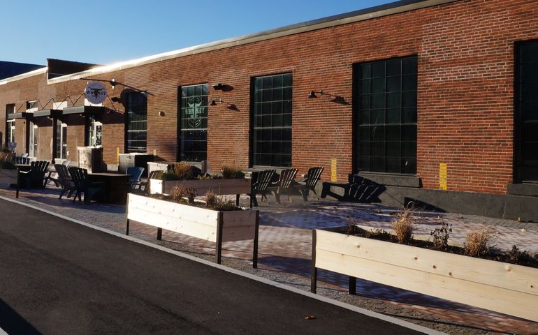 A long one-story brick building with a sign that says Whiskey Barrell over one door and a patio with empty chairs.