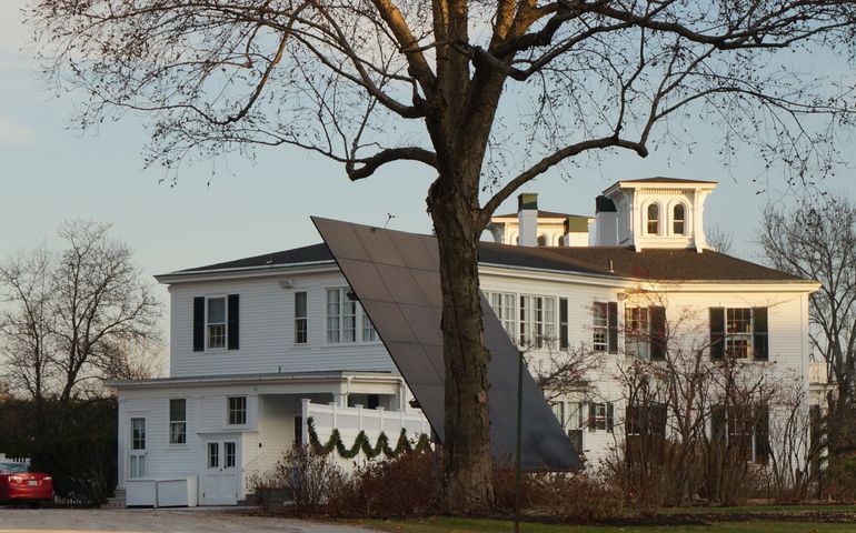 A white federal style house with a large solar panel in the yard