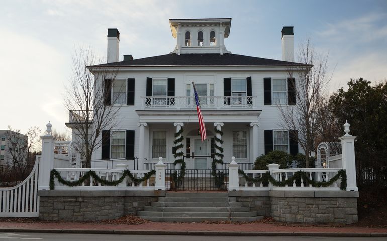 A white federal style house with Christmas evergreen bunting and an American flag