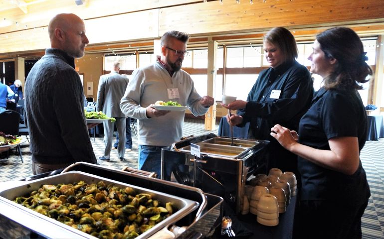 A woman serves food at a buffet to two men and another woman.