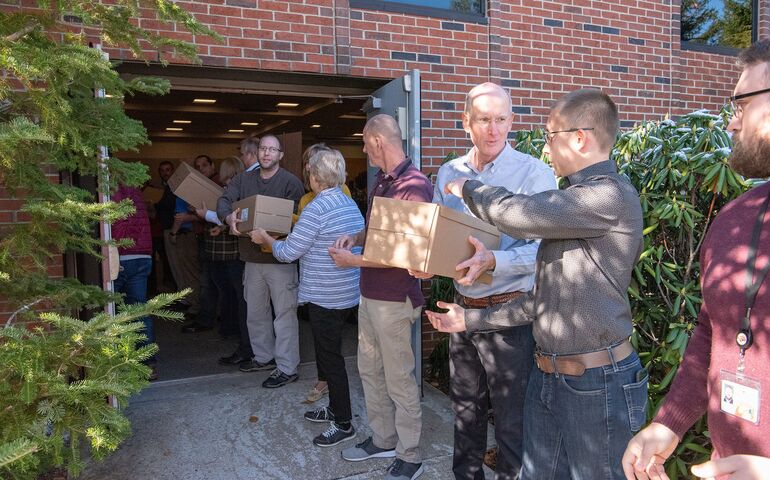 A line of people carrying boxes into a building.