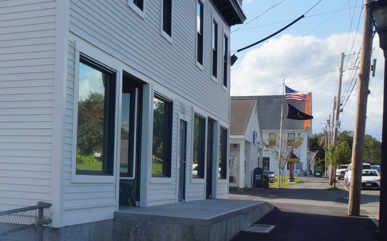 A small town main street with wooden buildings and an American flag flying in front of the post office