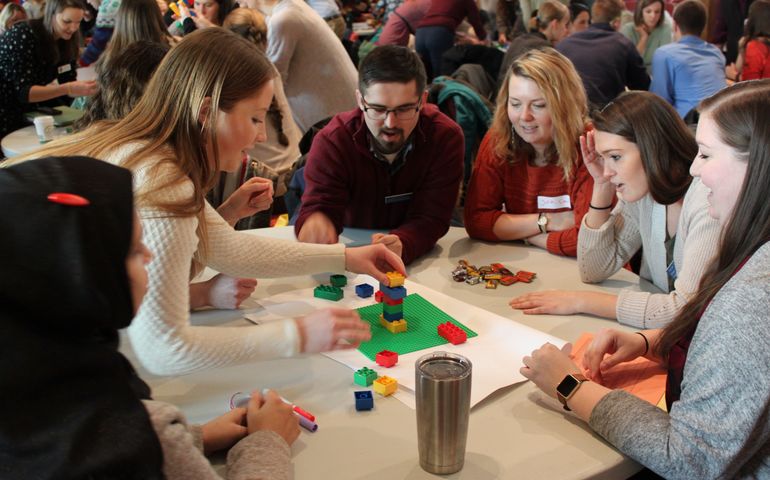 UNE students from seven health professionals at a table in a learning exercise.