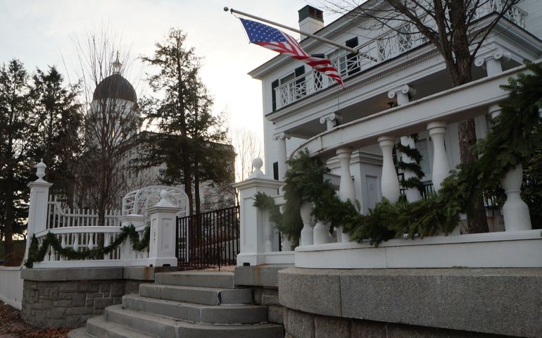 The maine state house in the background, with a white colonial house with an american flag flying in the foreground