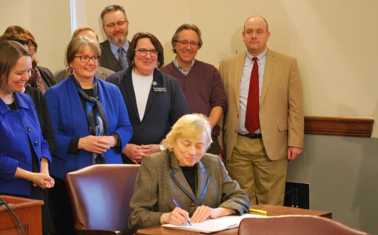 Gov. Janet Mills surrounded by lawmakers signing a bill.