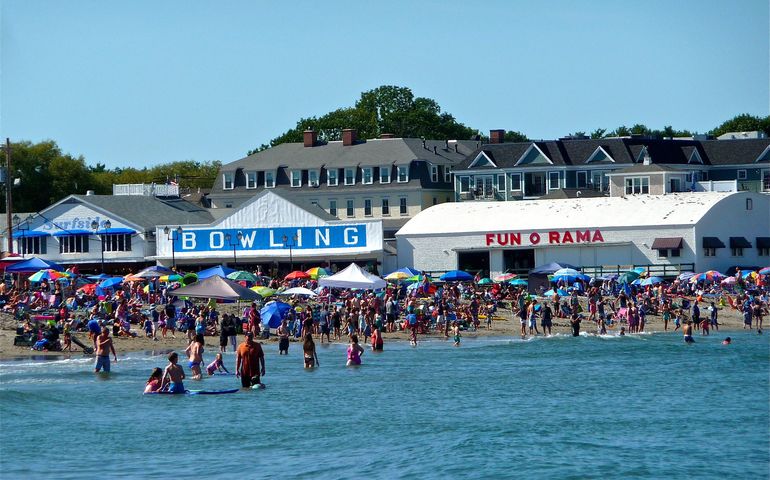 beach with people in surf and storefronts, arcades and hotels beyond