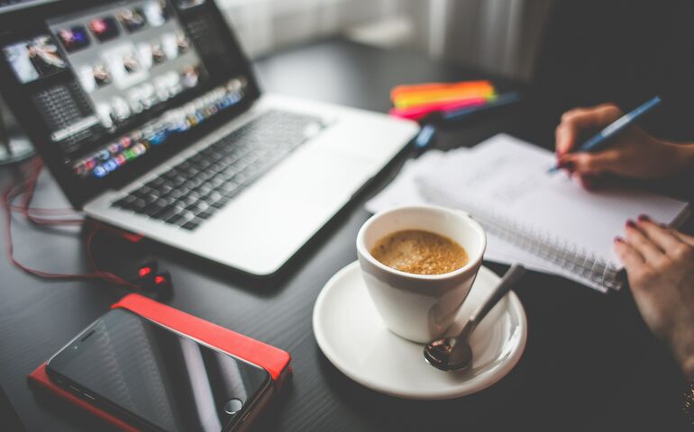 Stock photo showing a work station at home with a laptop, phone, notebook and coffee cup 