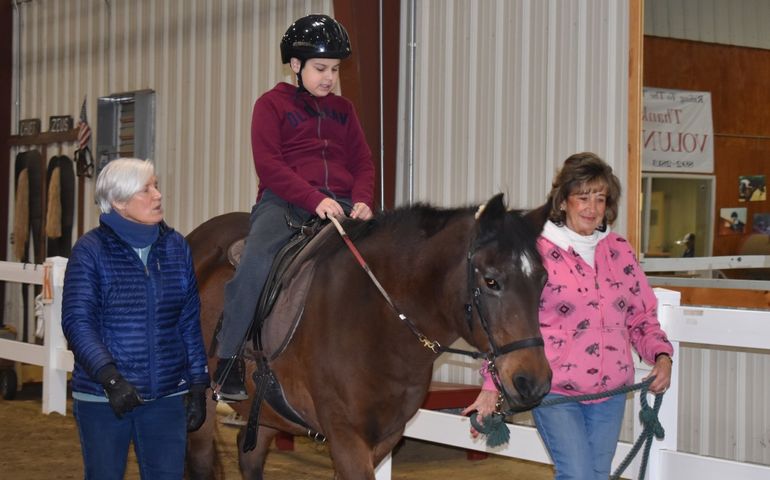 Photo of child on a horse at Riding to the Top, accompanied by trainers.
