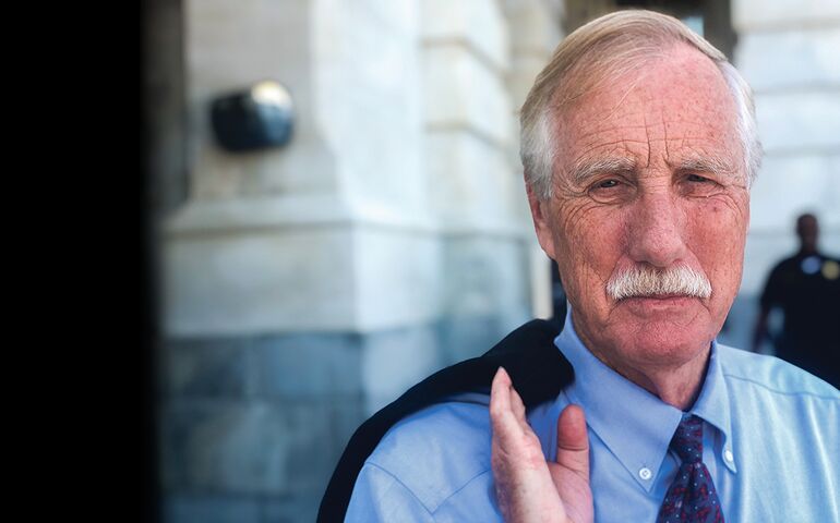 Sen. Angus King with white hair and a mustache portrait photo with a jacket over his shoulder 