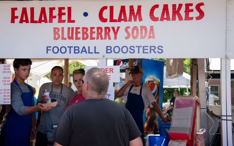 a group of people at a festival booth advertising blueberry lemonade