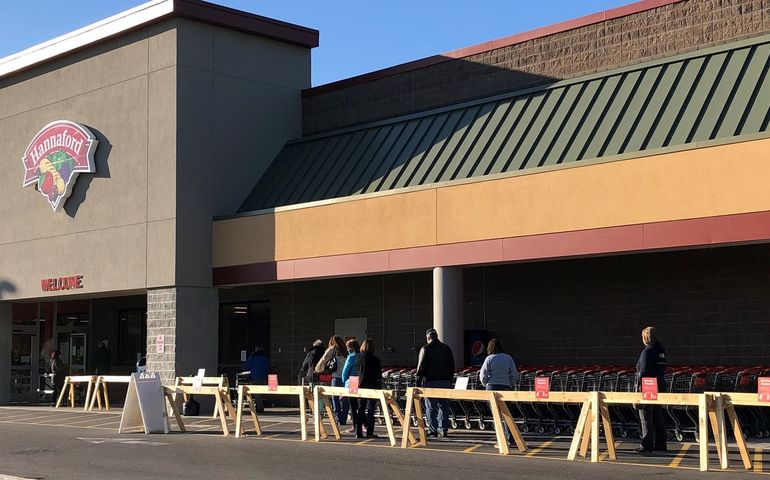 A line of people outside a grocery store wearing masks