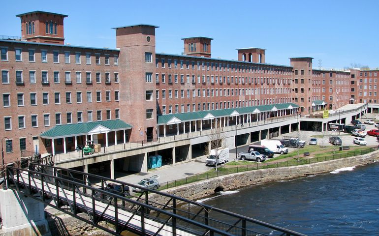 A long brick mill on a river with a green awning above the first floor
