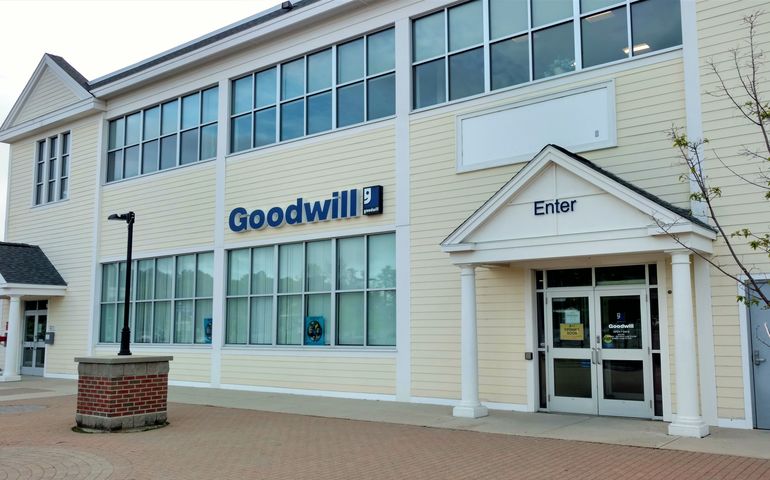 A two story pale yellow building with a sign above the door that says goodwill