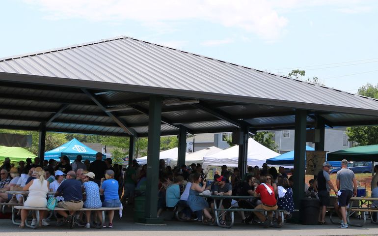 Many people sitting at picnic tables on a pavilion in a park