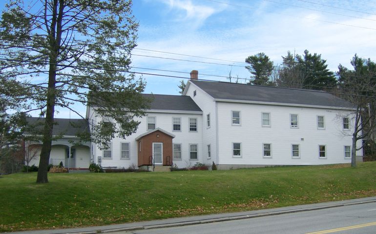 two-story white residential building, with trees nearby