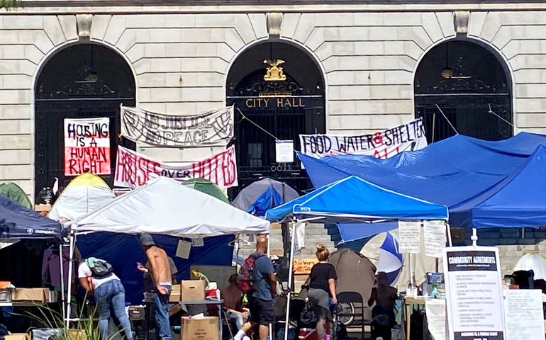 a line of tents with signs that say things like housing is a human right are set up in front of Portland city hall, a large granit building