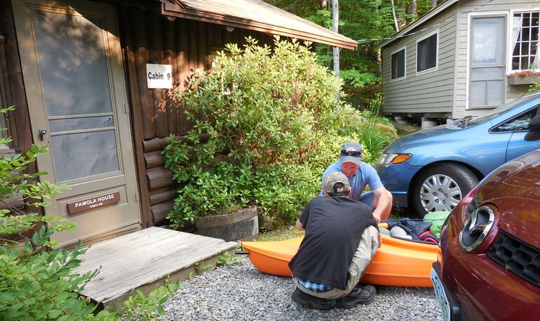 A man and a teenage boy back belongings into a kayak on the ground in front of a cabin