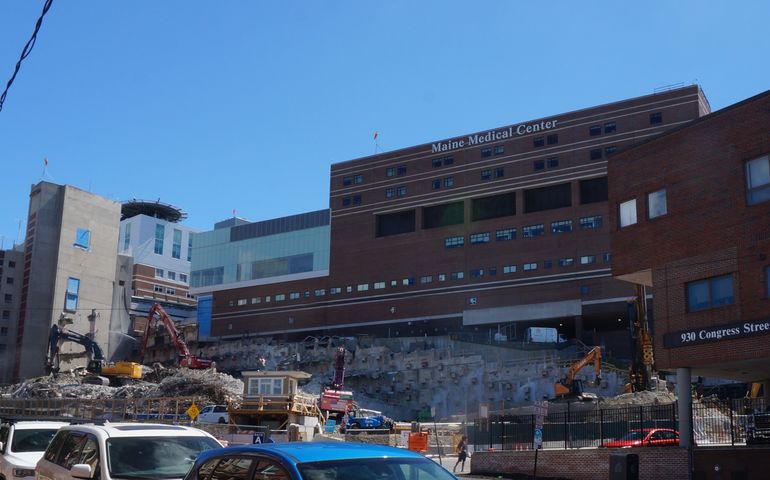 a pile of rubble and some bulldozers in front of a big brick building that says Maine Medical Center