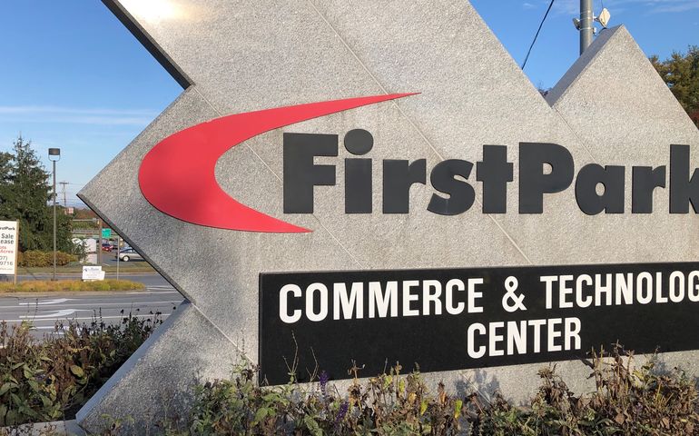 A large sign made of granite that says FirstPark commerce & technology center with a smaller sign in the background that says lots for sale or lease