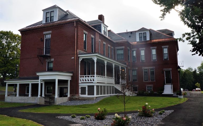 A 19th century brick two-story building with white trim and nicely landscaped lawn