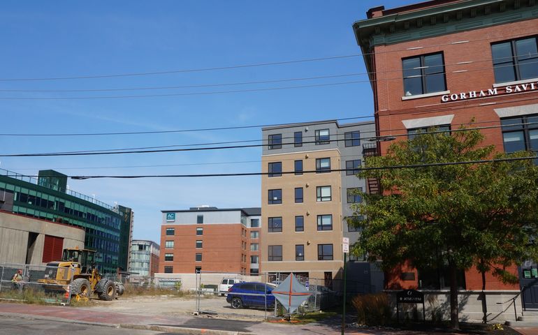 A vacant lot with modern buildings in the background and a renovated brick building to the right