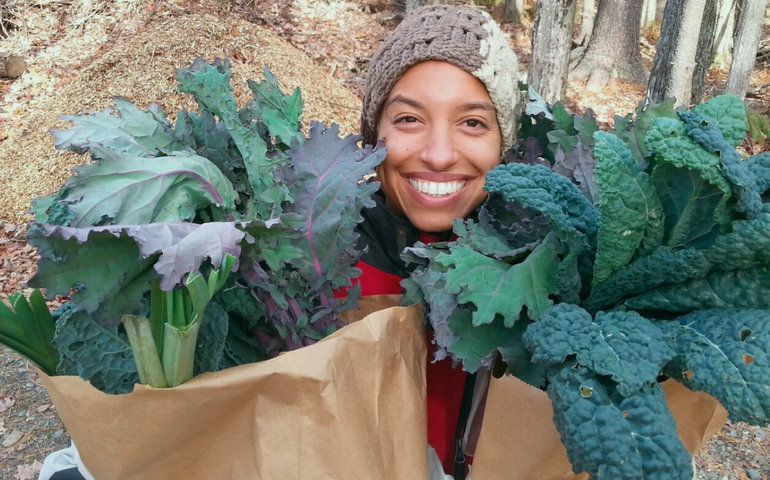 Leah Penniman, a woman smiling holding bags of a lush green crop