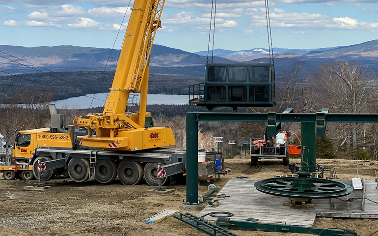 A crane removes parts of a ski lift while a vista of mountains is the backdrop