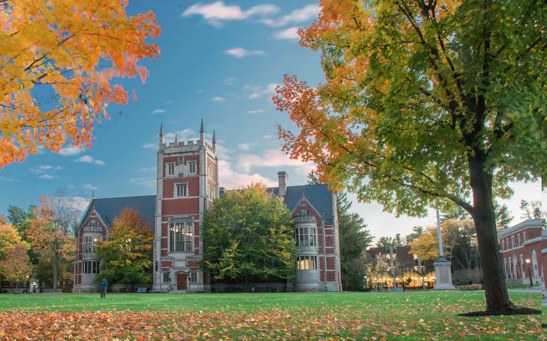 A victorian brick building with a tower on a wide lawn with fall foliage on the trees