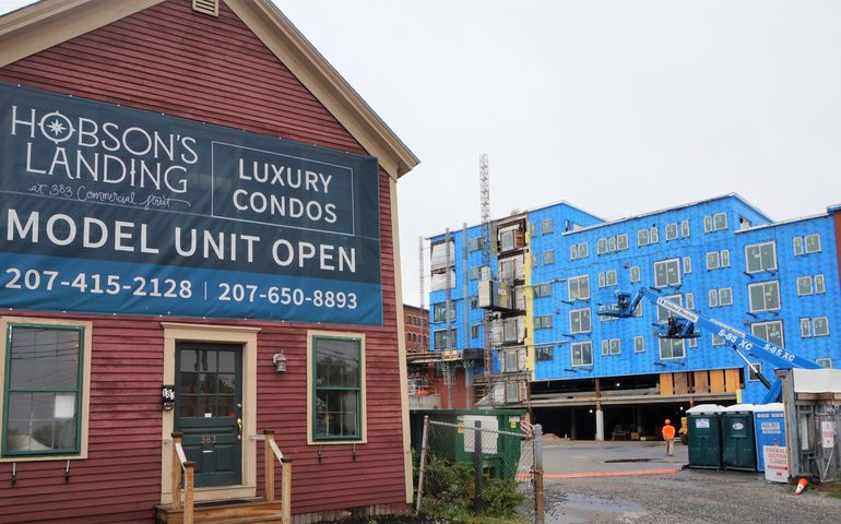 an small very old wooden building with a sign that says hobson's landing luxury condominiums, with a large construction project going on behind it