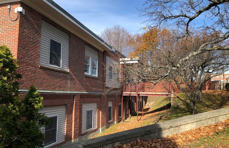 A brick building faceing a hill, with a walkway going from the street to a door on the second floor.