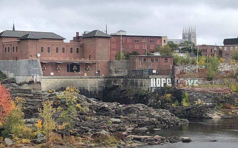 A river with rocks and foliage in the foreground with mills and church spires beyond "hope" and "love" are painted in large letters on the rocks above the river