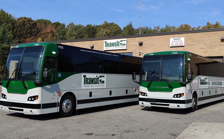 Two green and white large buses with signs that say transit biddeford saco old orchard beach