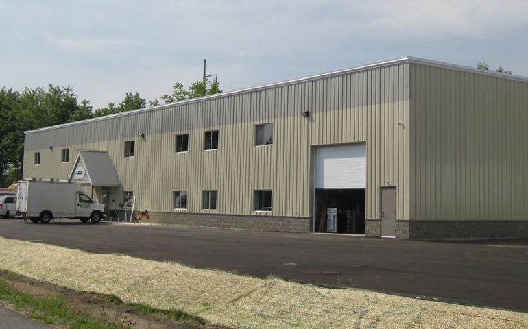 a new looking industrial building with a truck pulled up to one bay and grass seeding on a strip in front of a parking lot
