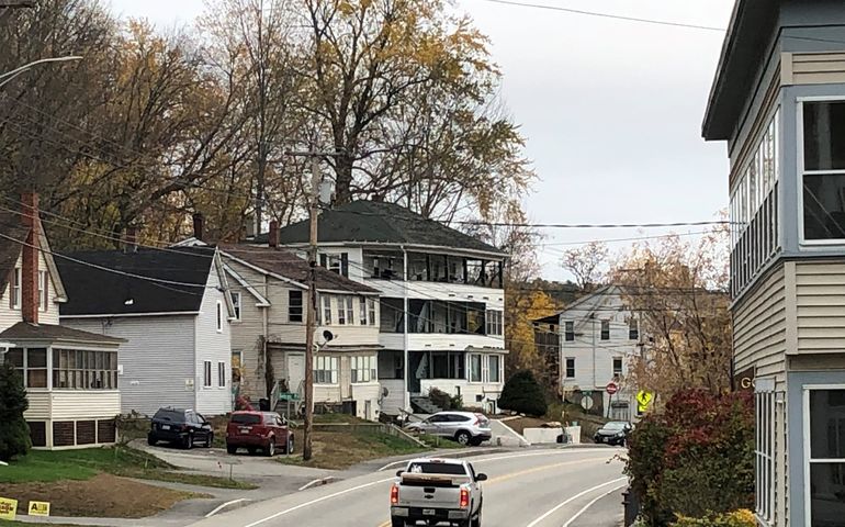 a pickup truck drives down a two lane street with triple deckers and multi family houses on either side