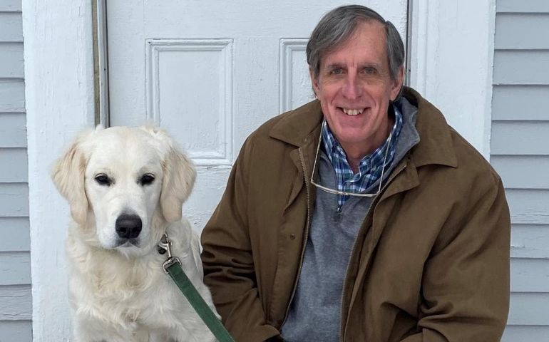 a smiling man sitting on steps outdoors next to a white labrador retriever