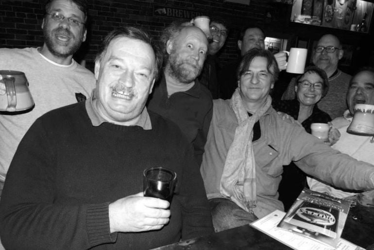 a black and white photo of a group of people sitting at a bar and raising their mugs. they look like they've had a view