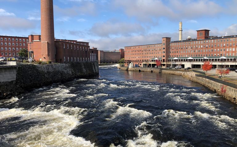 Several old brick mill buildings split by a roaring river