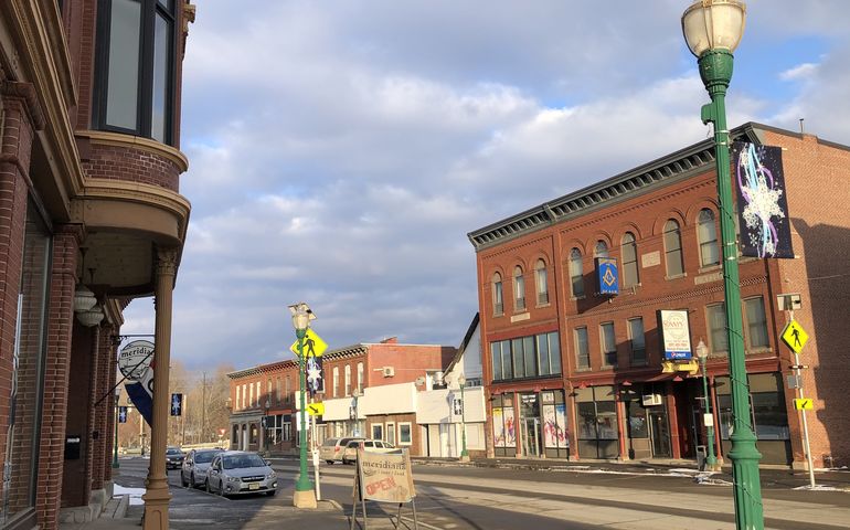 A small Main Street with a fancy victorian brick building up close on the left and a row of two-story brick commercial buildings across the street