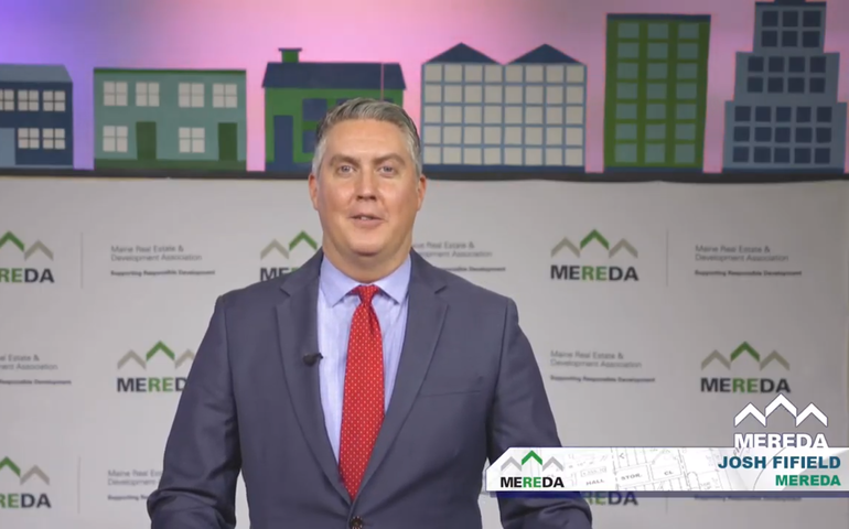 A man in a suit stands in front of a background that says MEREDA
