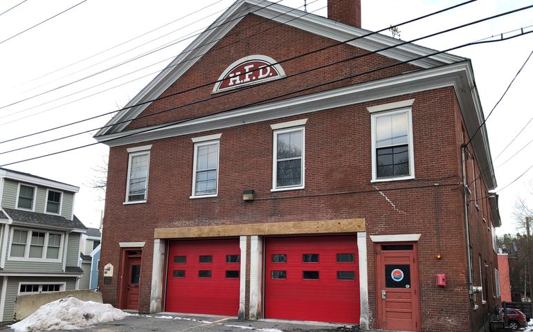 an old brick building with two bright red bay doors in front and smaller walk-in doors on either side, windows above and HFD in the peak near the roof